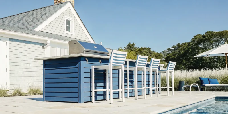 Outdoor kitchen design by Long Island contractors featuring blue cabinetry, a stainless grill, and poolside seating.