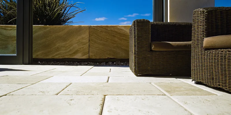 Travertine brick floor on an outdoor patio with wicker furniture and a stone planter.