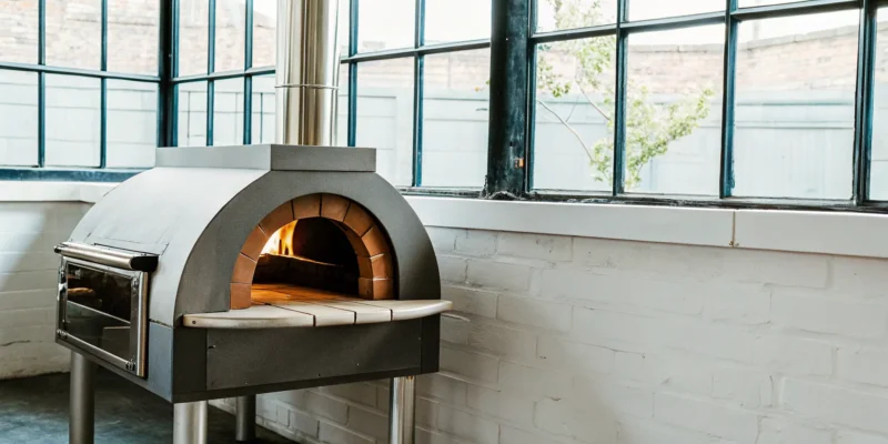 Rossofuoco Clessidra wood-fired oven with a modern stainless steel design and a fire burning inside.