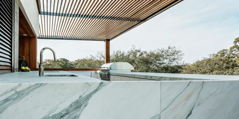 White marble countertops in a modern outdoor kitchen with a built-in grill and sink.