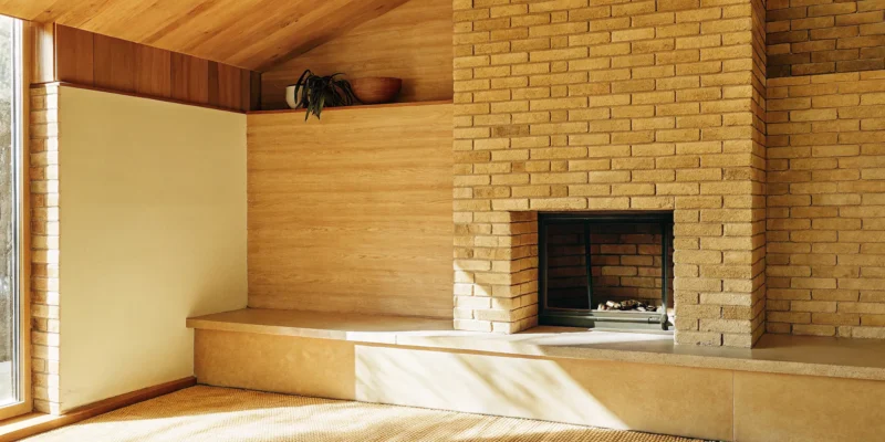 Modern brick corner fireplace design with light earthy tones and a built-in shelf.