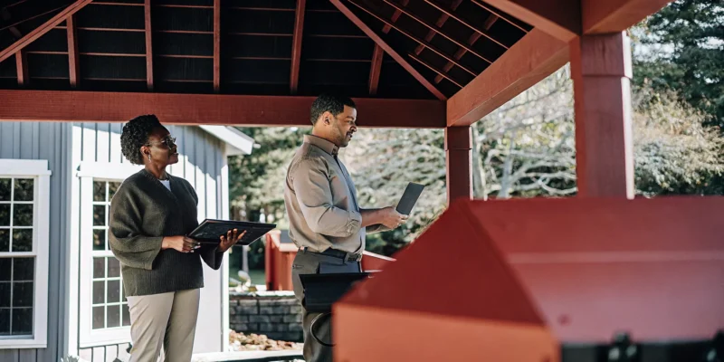 A Smithtown pavilion builder reviews custom plans with a client under a new wooden pavilion.