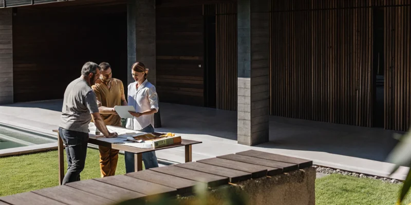 Homeowners reviewing inground pool plans with builders in their backyard.