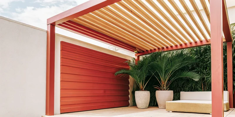 Modern red louvered roof pergola with adjustable slats shading a patio seating area.