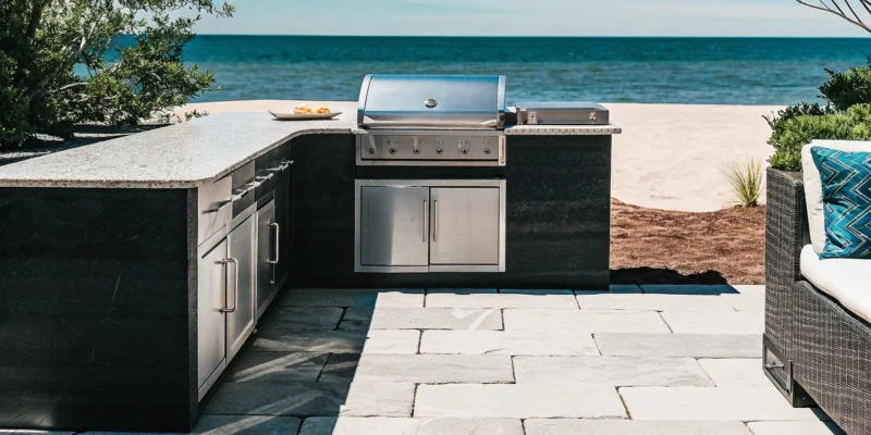 Weatherproof outdoor kitchen cabinets with stainless steel grill and stone veneer on a Long Island bluestone patio