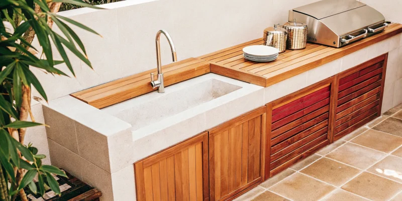 Simple outdoor kitchen idea with a built-in grill, sink, and wooden cabinets.