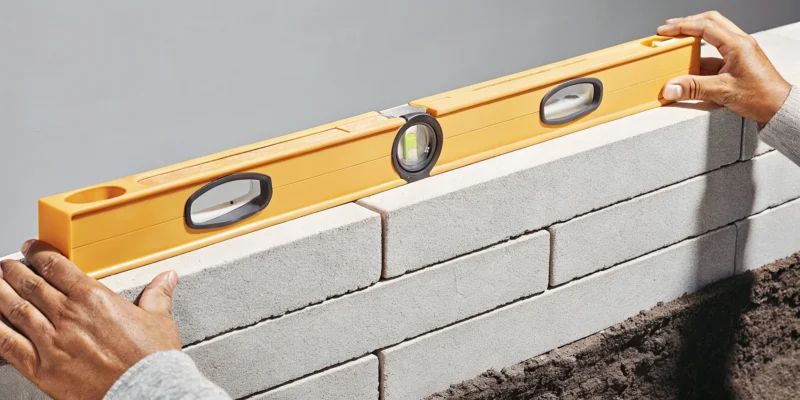 Using a level to align a course of interlocking retaining wall blocks.