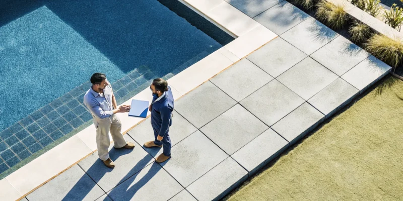 A contractor discusses porcelain paver installation options with a homeowner by a pool.