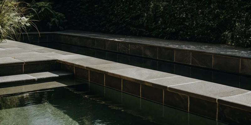 Light-colored natural stone coping surrounding a backyard pool on Long Island.